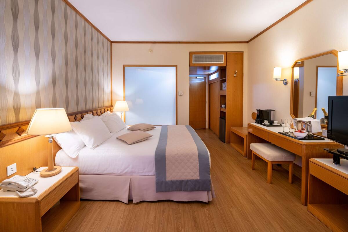 Ein Hotelzimmer mit Bett, Nachttischlampen, einem Schreibtisch mit Fernseher, einem Spiegel und einem durchgegangenen Tür angedeuteten Badezimmer.