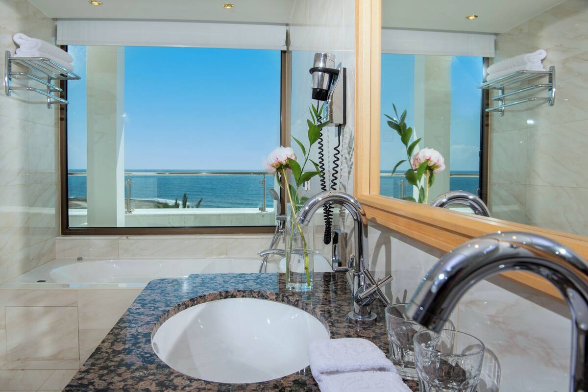 Ein Badezimmer mit großem Fenster, einer Badewanne, einem Waschbecken und einem Spiegel.