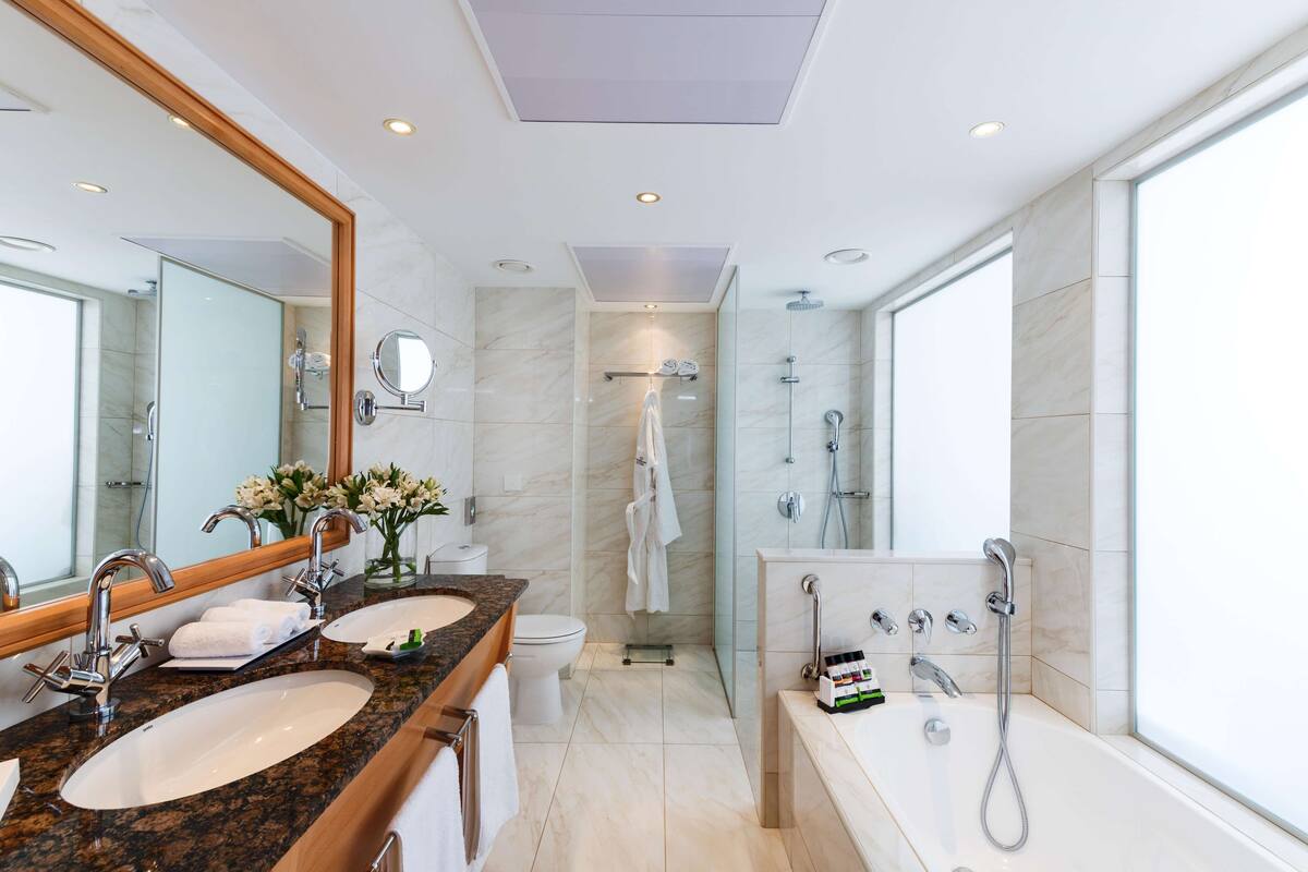 Ein modernes Badezimmer mit zwei Waschbecken, einem großen Spiegel, einer Badewanne und einer Dusche.