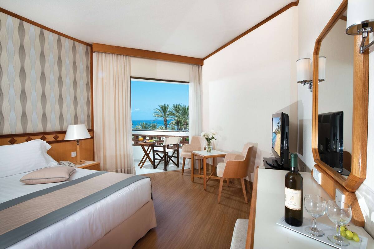 Ein Hotelzimmer mit Bett, Schreibtisch mit Stuhl, Fernseher und einer Flasche Wein, mit Blick auf den Ozean.