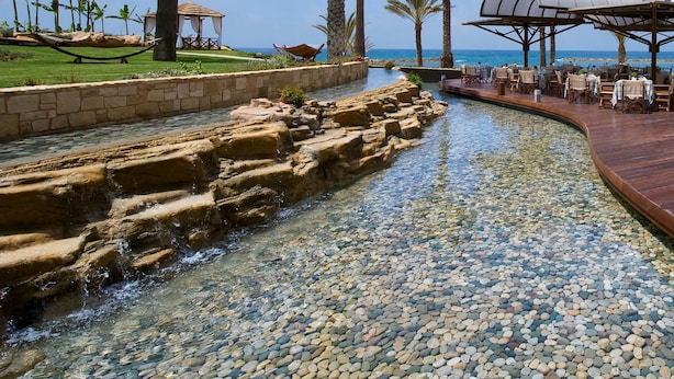 Ein ruhiger Urlaubsort mit klarem Pool, Palmen und einer Essgelegenheit mit Blick auf das Meer.