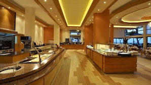 Eine Hotelhalle mit einem Buffetbereich, einer Kaffeestation und einer Sitzecke mit Tischen und Stühlen.