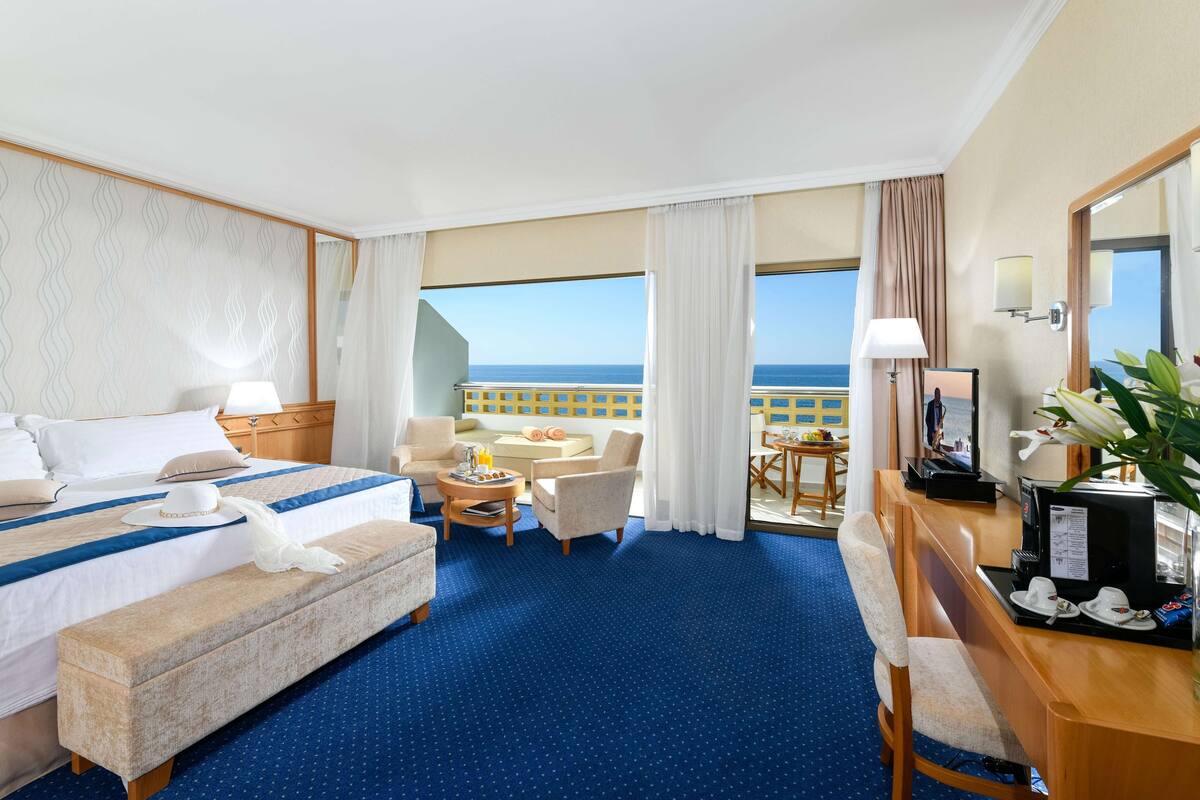 Ein Hotelzimmer mit Bett, Schreibtisch, Stuhl, kleinem Tisch und Meerblick.