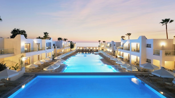 Un hotel moderno con piscina central, varios balcones y palmeras.