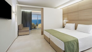 Habitación de hotel moderna con una cama grande, un sofá y un televisor. Tiene un balcón con vista al mar.