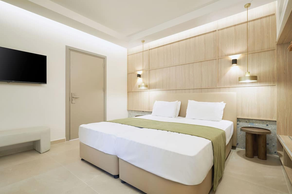 A modern hotel room with a large bed, a bench, a flat-screen TV, and a wooden panel wall.