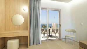 Una habitación moderna con un ventanal corredero que da a un balcón con mesa y sillas, un espejo redondo y un banco de color claro.