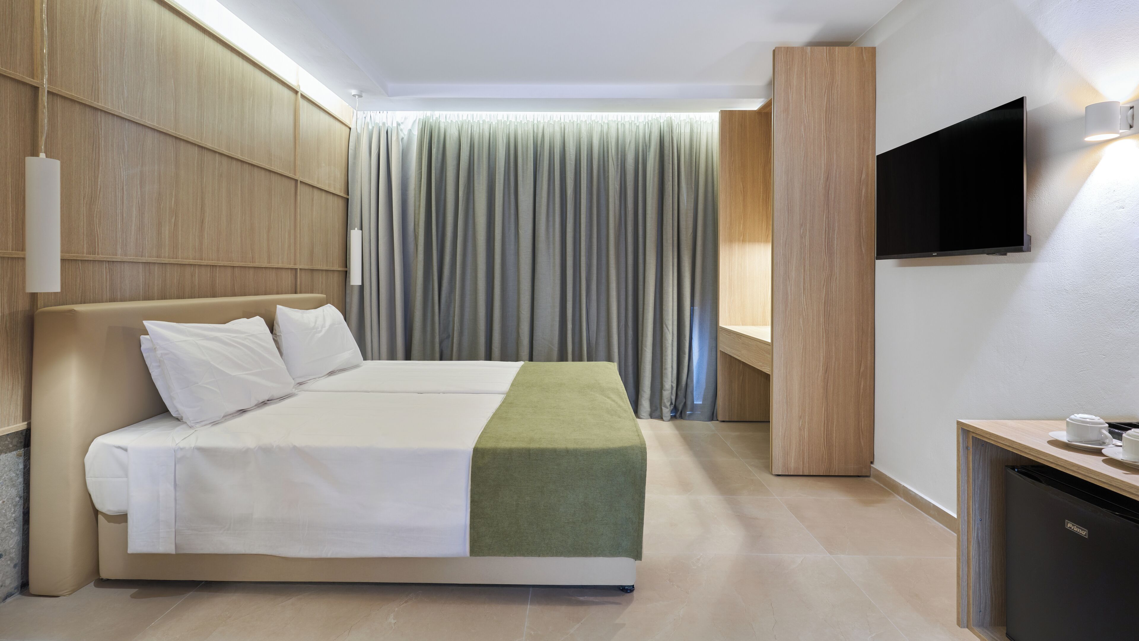 A hotel room with a bed, a TV, a desk, and a curtain.