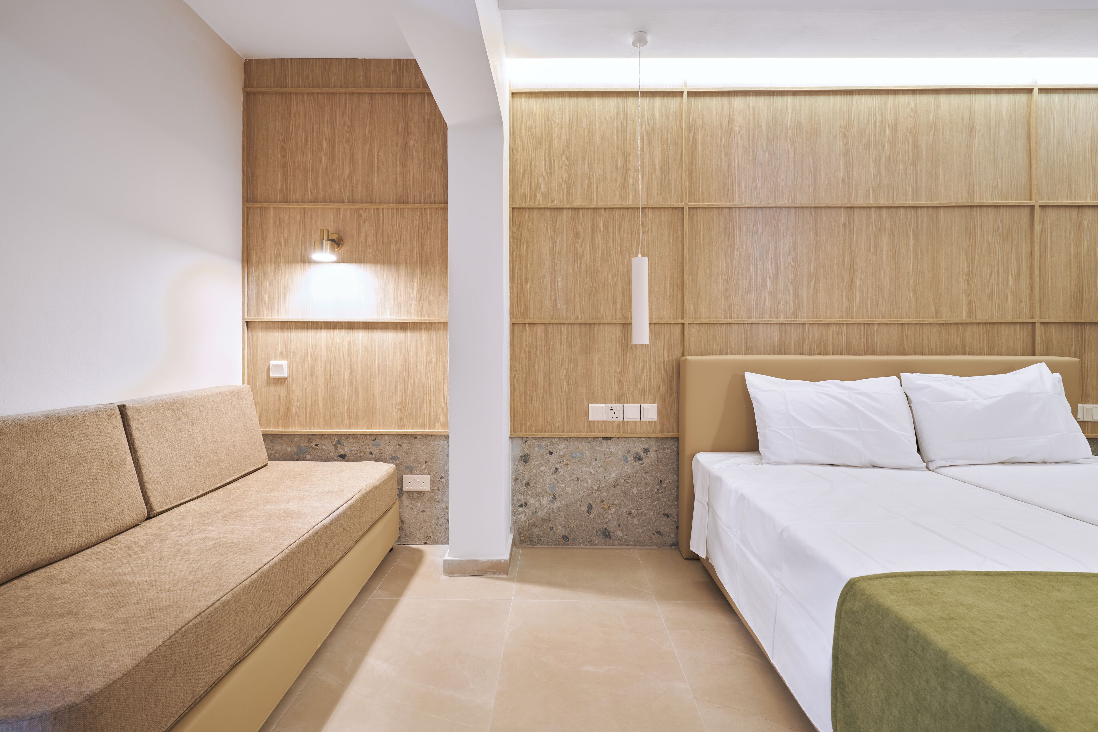 Een moderne hotelkamer met een wand van houtpaneel, een beige sofa en een bed met witte lakens.