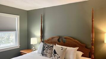 Une chambre à coucher avec un grand lit, une tête de lit en bois, deux lampes fixées au mur et une fenêtre avec des stores.