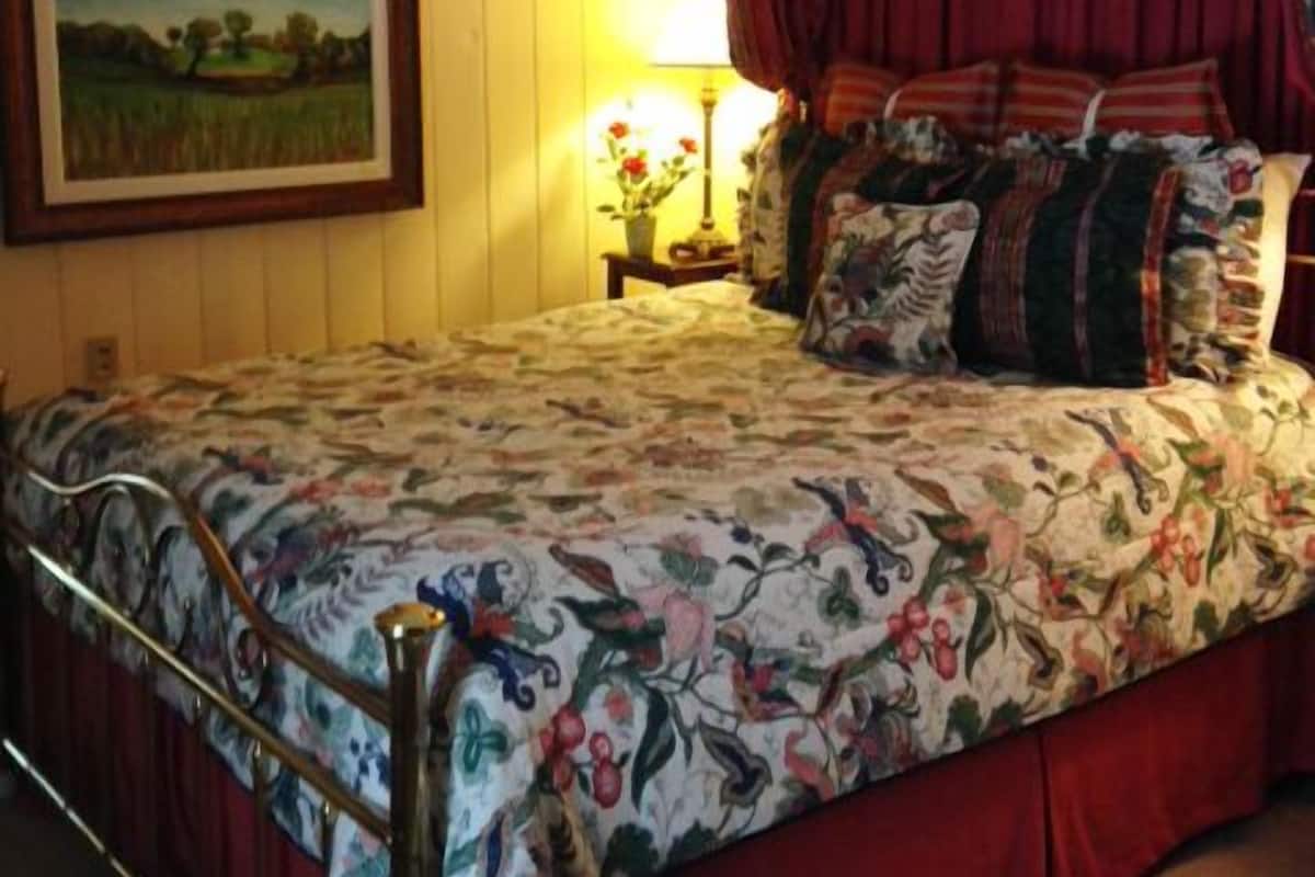 A bedroom with a floral bedspread, a painting on the wall, a lamp, and a red-striped canopy over the bed.
