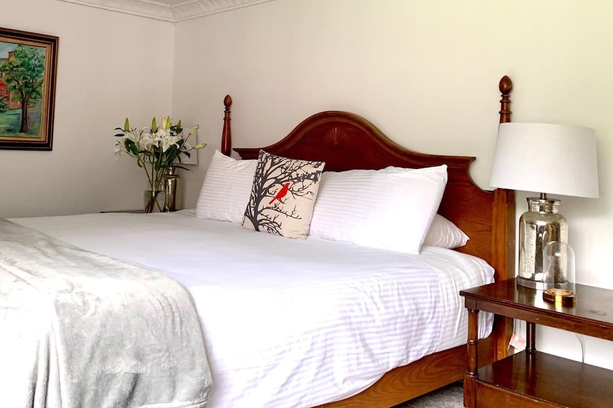 A neatly made bed with white linens, a wooden headboard, and a bedside table with a lamp.