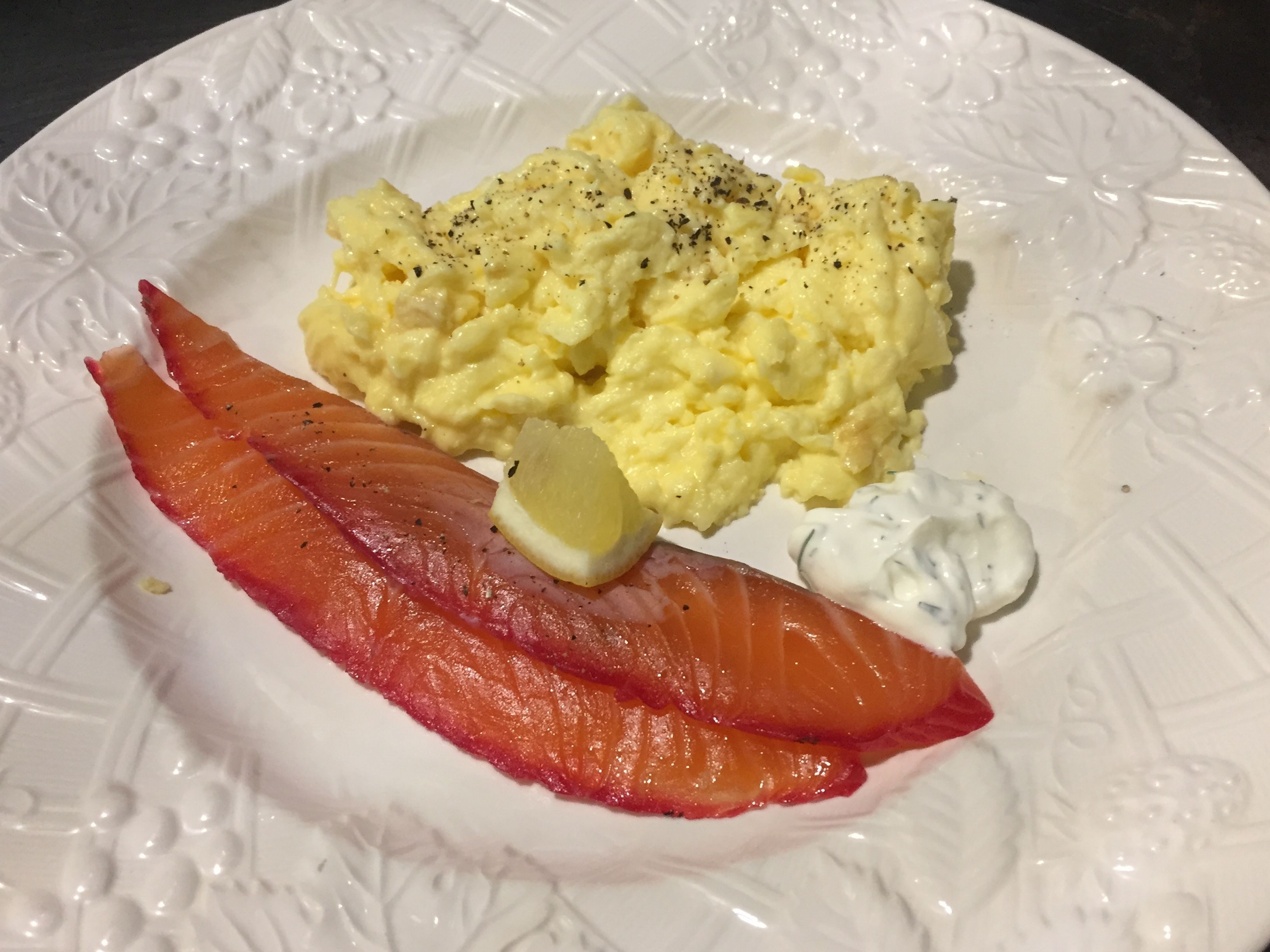 Un plato con huevos revueltos, salmón ahumado, un gajo de limón y una cucharada de crema agria.