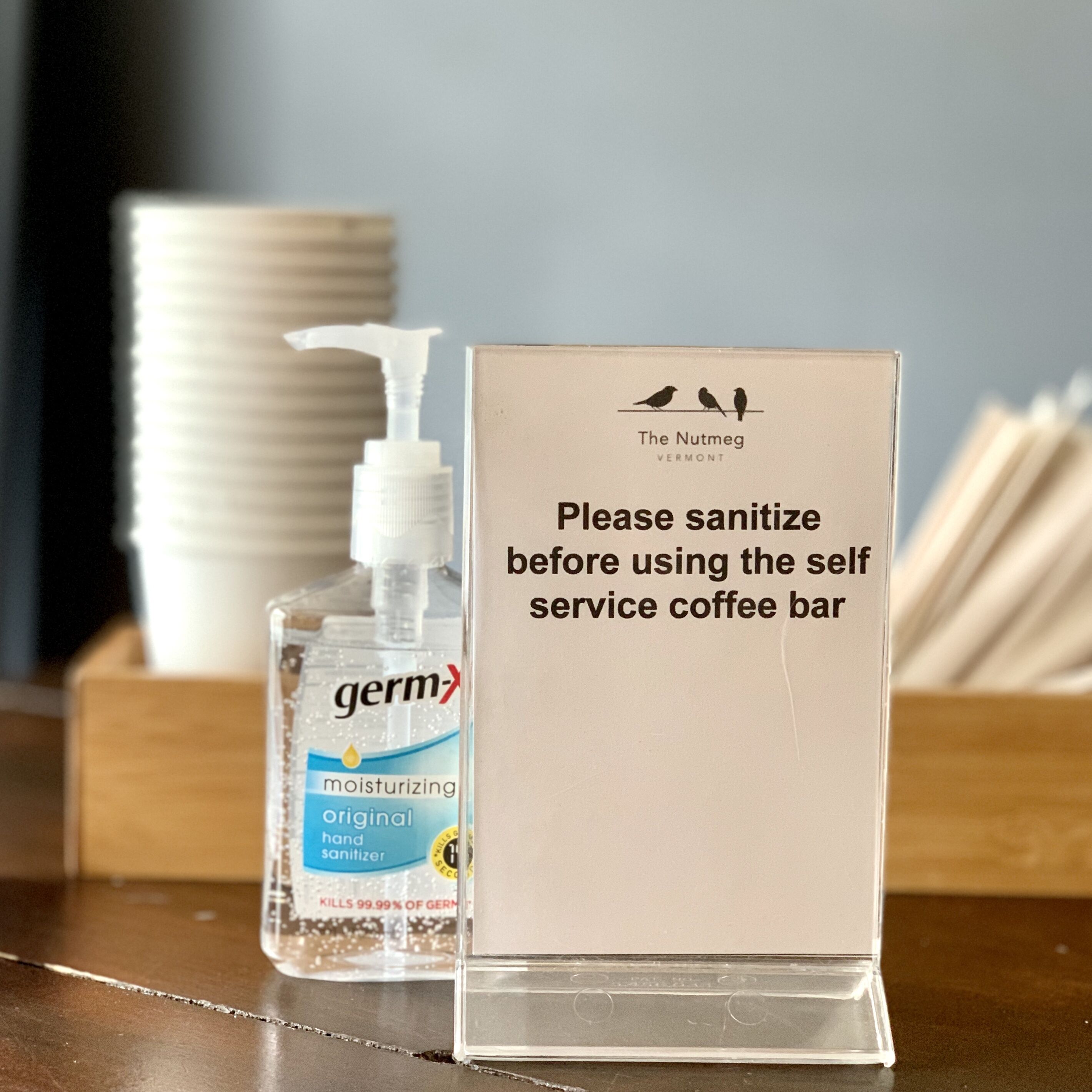 A germ-X hand sanitizer and a sign requesting guests to sanitize before using the self-service coffee bar.
