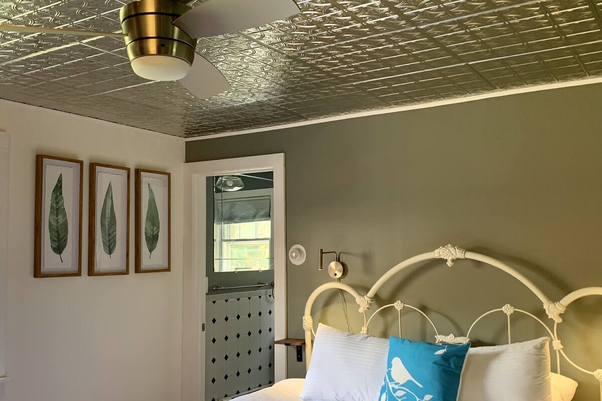 A bedroom with a bed, a ceiling fan, and framed botanical prints on the wall.