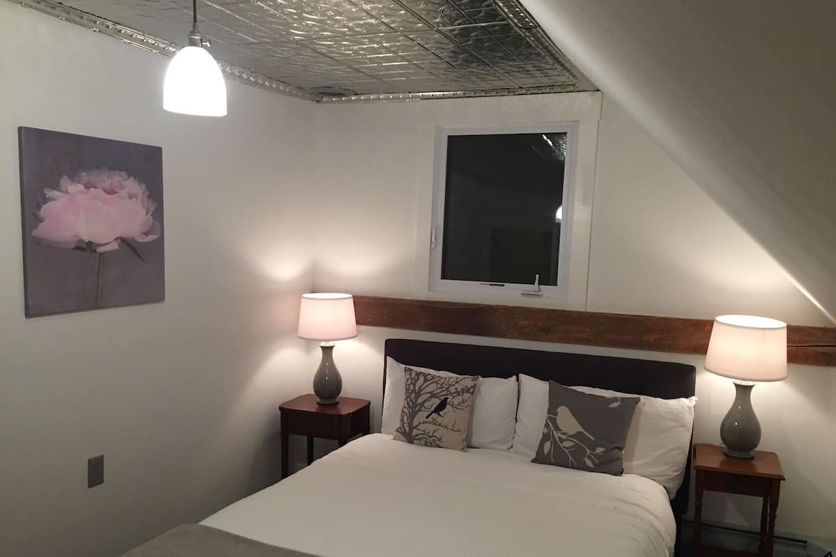 A bedroom with a bed, two bedside tables with lamps, a window, and a ceiling with a textured design.