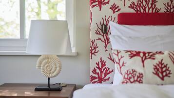 Een net opgemaakt bed met een rood-wit gebeddeken, een wit kussen en een witte lamp op een houten nachtkastje.