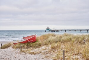 Ein Strand mit einem roten Boot, einer Anlegestelle und einer Kuppelstruktur im Hintergrund.