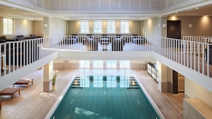 Una piscina interior amplia con un balcón y zona de estar en el segundo piso.