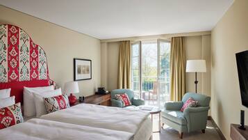 A hotel room with two beds, a sitting area with a chair and a table, a TV, and a large window with curtains.