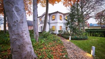 A building with a symmetrical facade, multiple windows, and a well-maintained garden with a pathway.