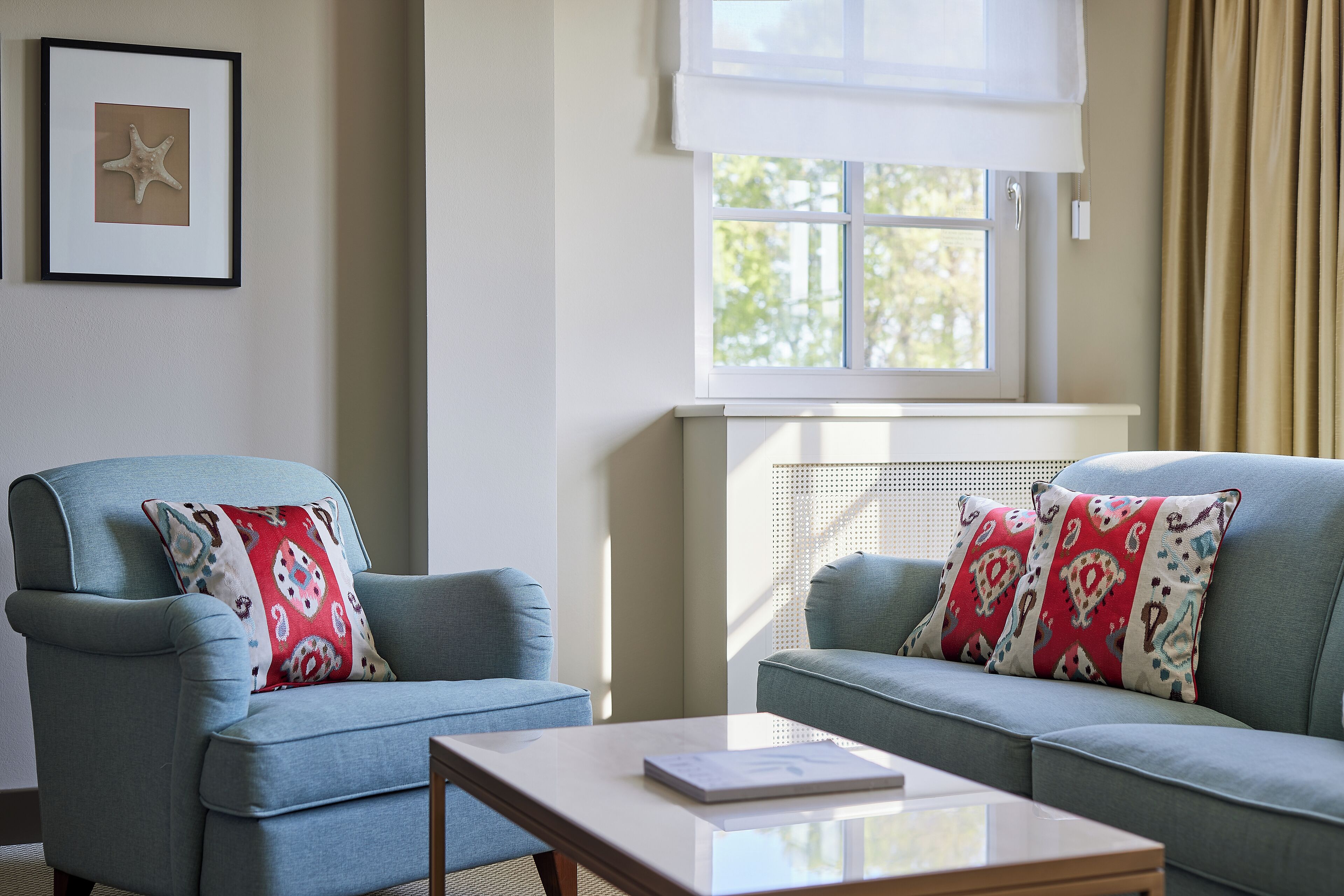 A room with two light blue armchairs, a white coffee table, and a window with a white blind.