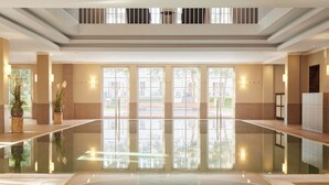 Una amplia piscina cubierta con paredes de vidrio transparente que permiten vistas al exterior. Hay plantas en macetas e iluminación empotrada en las paredes.