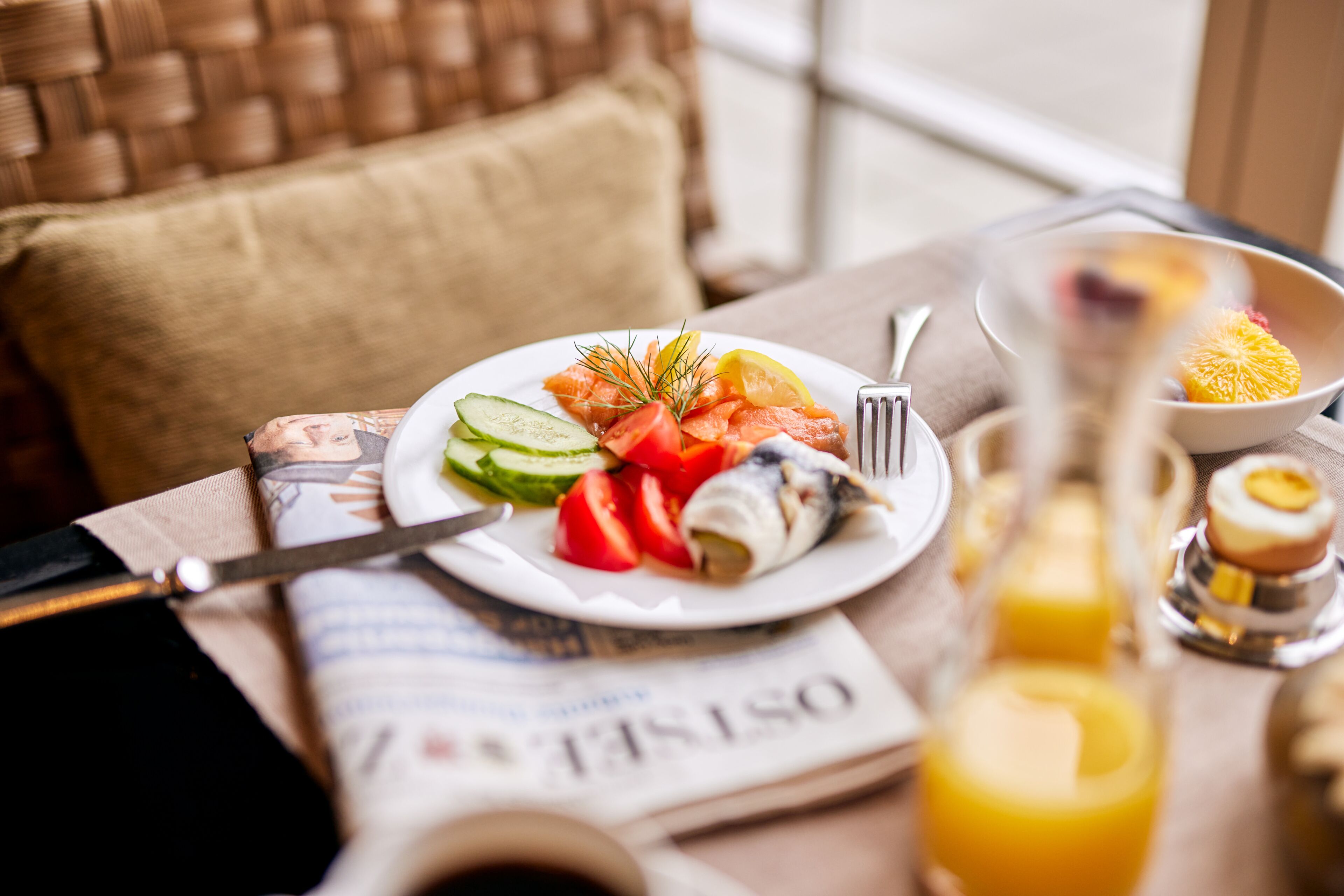 A breakfast setting with a plate of food, a newspaper, a glass of orange juice, and a fork on a table.
