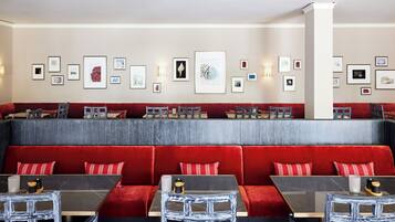 Een restaurant met rode bekleden zitbanken, zwart-witte stoelen en een muur versierd met ingelijste kunstwerken.