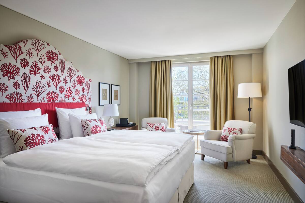 Ein Hotelzimmer mit einem großen Bett, zwei Sessel, einem kleinen Tisch, einer Lampe und einem Fernseher.