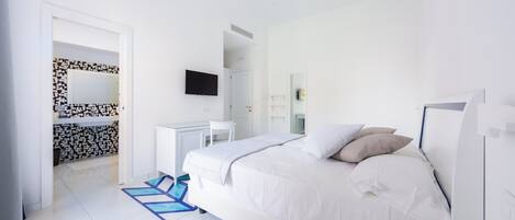 Una habitación de hotel moderna con una cama grande, un escritorio, un televisor y un baño con pared estampada.