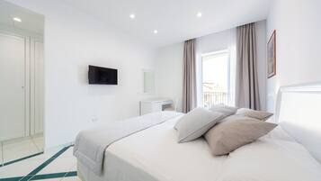 Ein modernes Hotelzimmer mit einem großen Bett, einem flachbildfernseher an der Wand, einem kleinen Schreibtisch und einem Fenster mit Vorhängen.