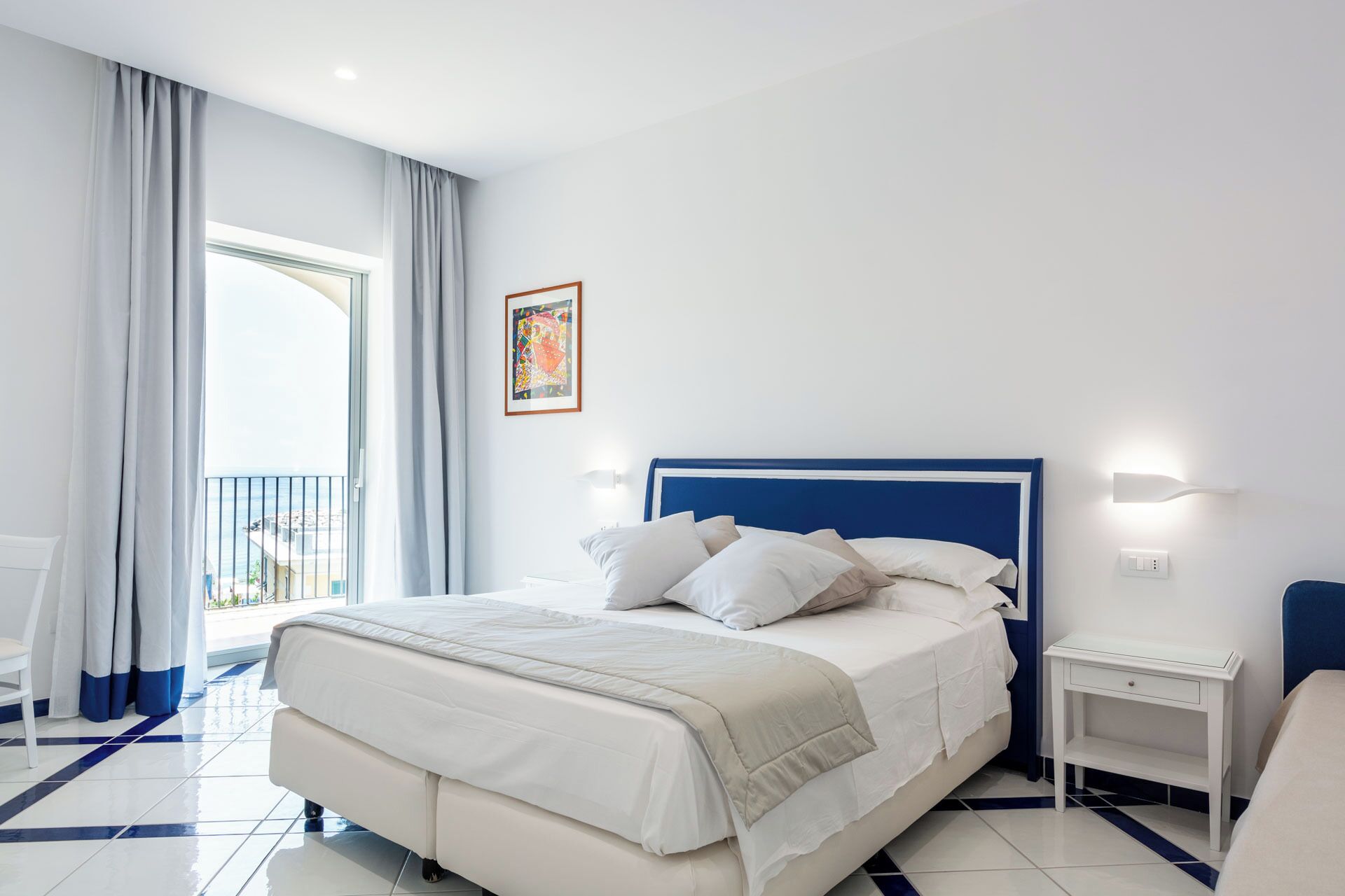 Een moderne hotelkamer met een groot bed, een nachtkastje en uitzicht op zee vanaf een balkon.