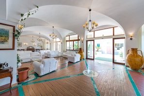Uma sala de estar espaçosa com sofás brancos, um vaso amarelo grande e piso de madeira com detalhes verdes.