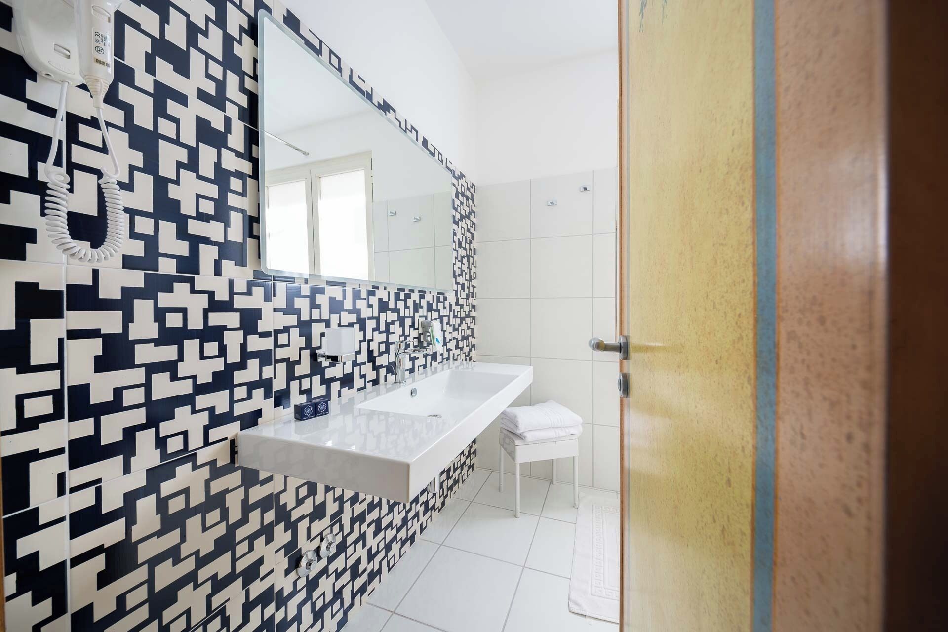 A modern bathroom with a geometric patterned tile backsplash, a white sink, and a large mirror.