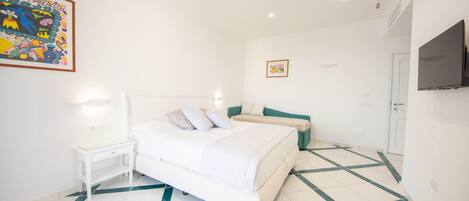 A bedroom with a large bed, a nightstand, a teal chair, and a television on the wall.