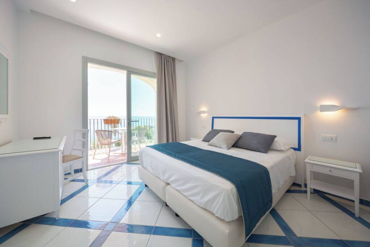 A hotel room with a bed, a desk, and a balcony with a view.