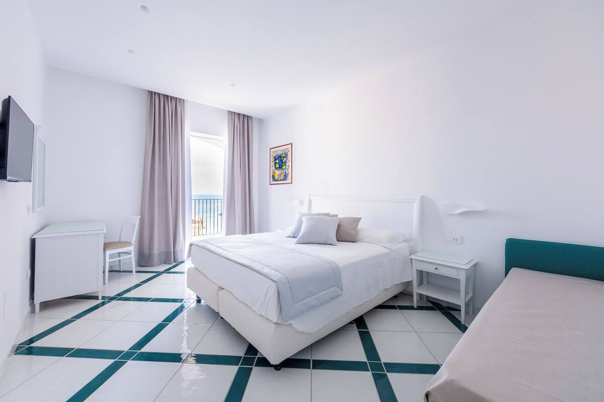 A hotel room with a bed, bedside table, chair, and a desk.