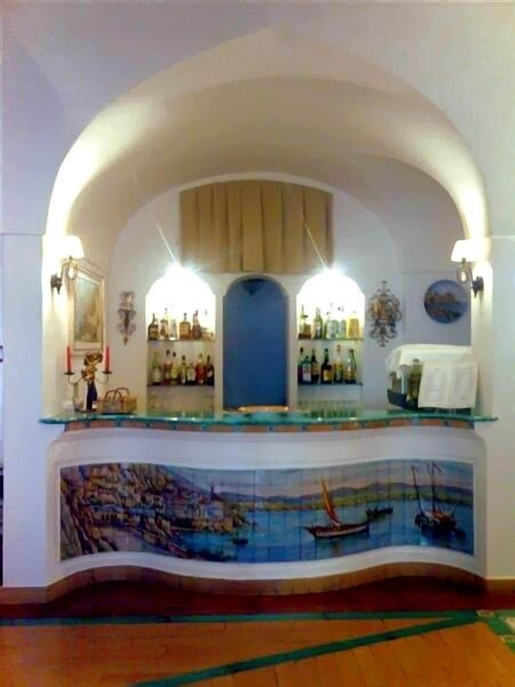 A bar area with a curved counter, a mural of a coastal scene, and a variety of bottles on shelves.