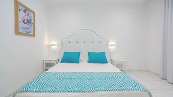 Un dormitorio con una cama blanca, dos almohadas turquesas, un cabecero blanco y un cuadro colgado en la pared.