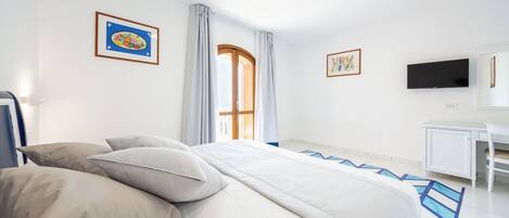 A hotel room with a bed, a desk, a television, and artwork on the walls.