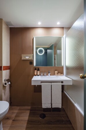 A bathroom with a white sink, mirror, and towel rack. There is a toilet to the left and a door to the right. - BYPILLOW Castellana (Madrid)