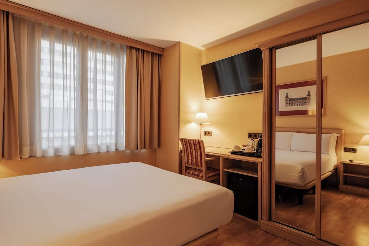 A hotel room with a large bed, a desk, a chair, a television, and a sliding door.