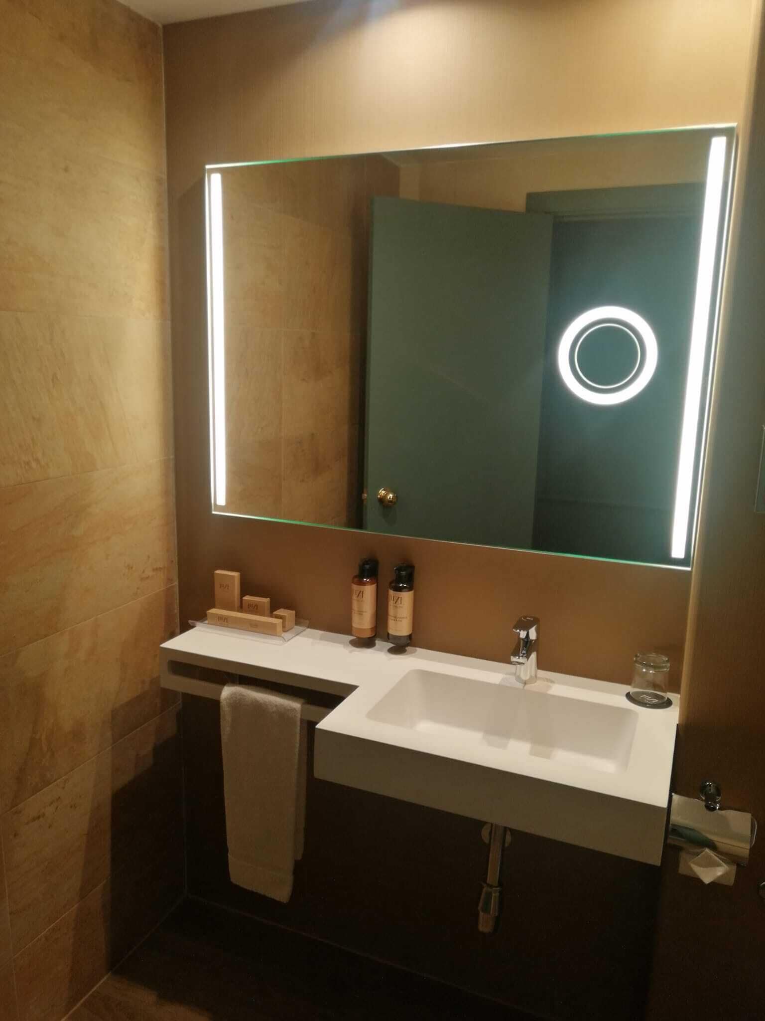 Un baño moderno con un espejo grande, dos lavamanos y un perchero para toallas.