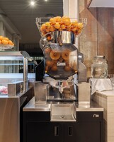 Ein Saftspender mit Orangen und einem mit 'Zümex' beschrifteten Glasbehälter, in einer gewerblichen Umgebung.
