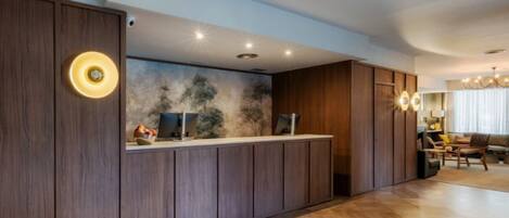 A reception area with a wooden reception desk, a wall-mounted computer, and a seating area with a chandelier.