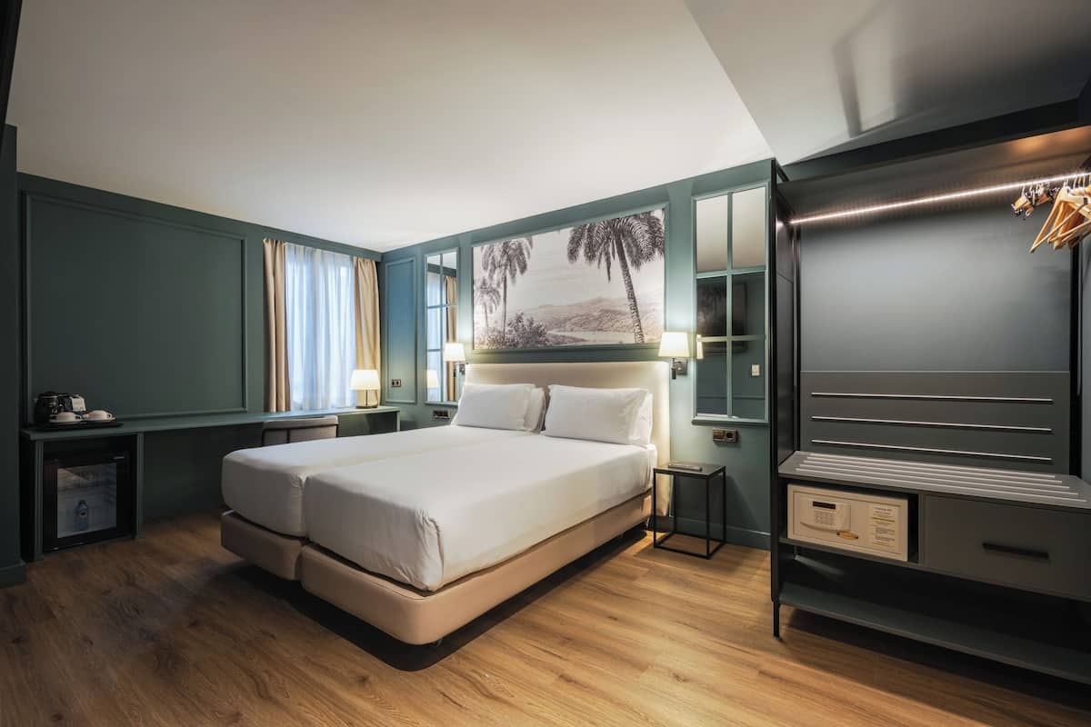 A modern hotel room with a large bed, a wardrobe, a desk, and a painting on the wall.