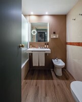 Ein modernes Badezimmer mit Holzboden, einem weißen Waschbecken, einem Bidet und einem Spiegel mit Beleuchtung.