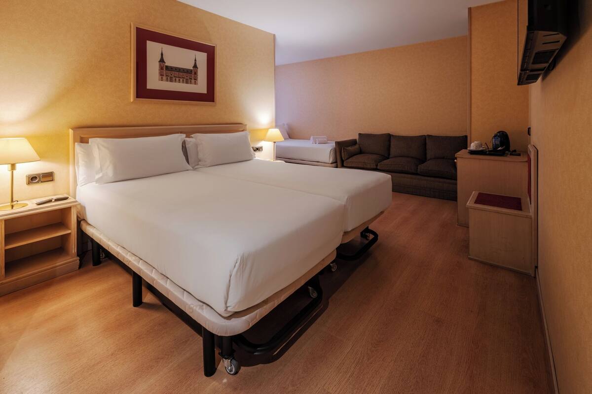 A hotel room with a large bed, a sofa, a desk, and a TV.