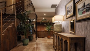 Um corredor com escadas de madeira, plantas em vasos, um console de madeira com abajur e quadros nas paredes.